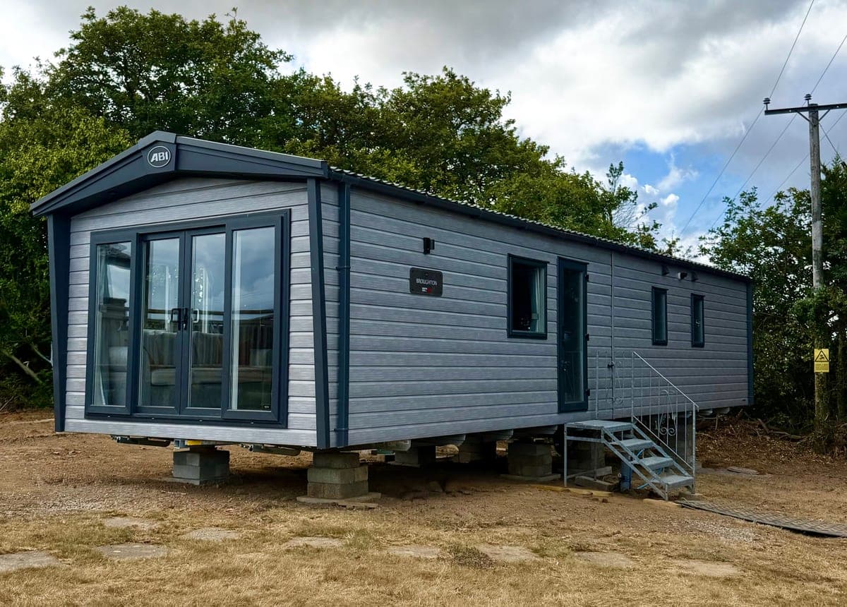 A new ABI Broughton holiday home on its pitch at Broadfield: grey, with glass doors at the front and metal steps up to the side door.