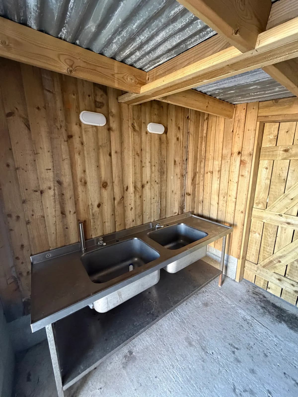 The washing up room: two stainless steel sinks on a steel stand, under a roof, with wooden walls and lights.